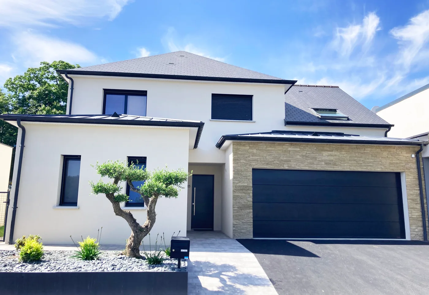 Maison à étage en enduit clair avec un pan de parement en pierre, toiture ardoise et double garage anthracite